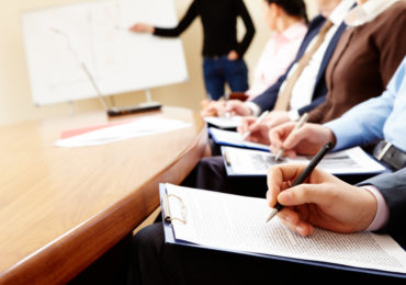 Close-up of businesspeople hands holding pens and papers near table at business seminar